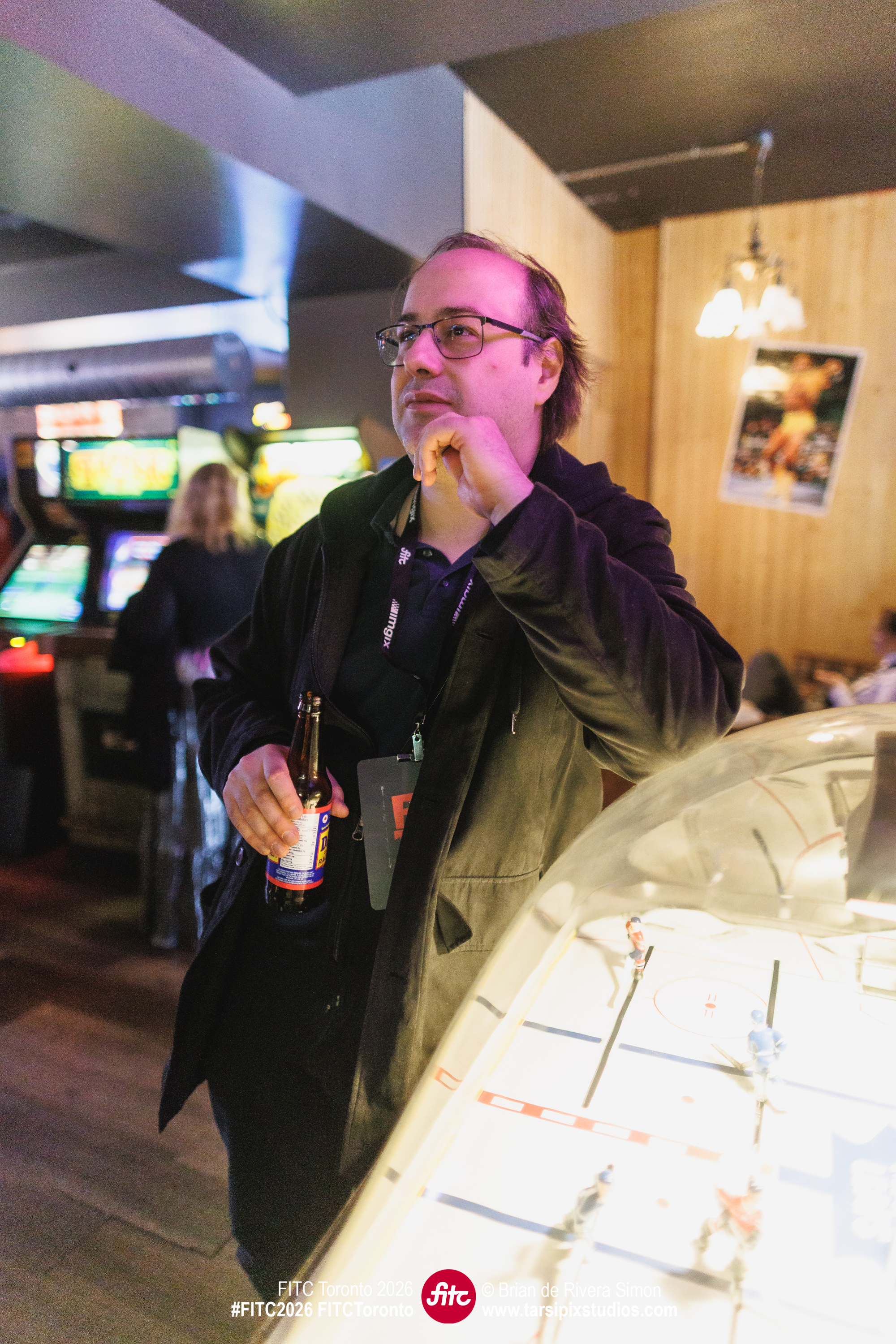 An image of David at an arcade with a bottle of root beer in his hand.